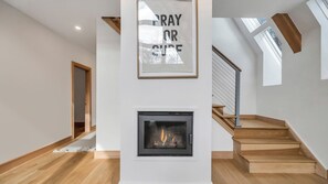 A modern interior with a fireplace, wooden staircase, and a framed sign above it.