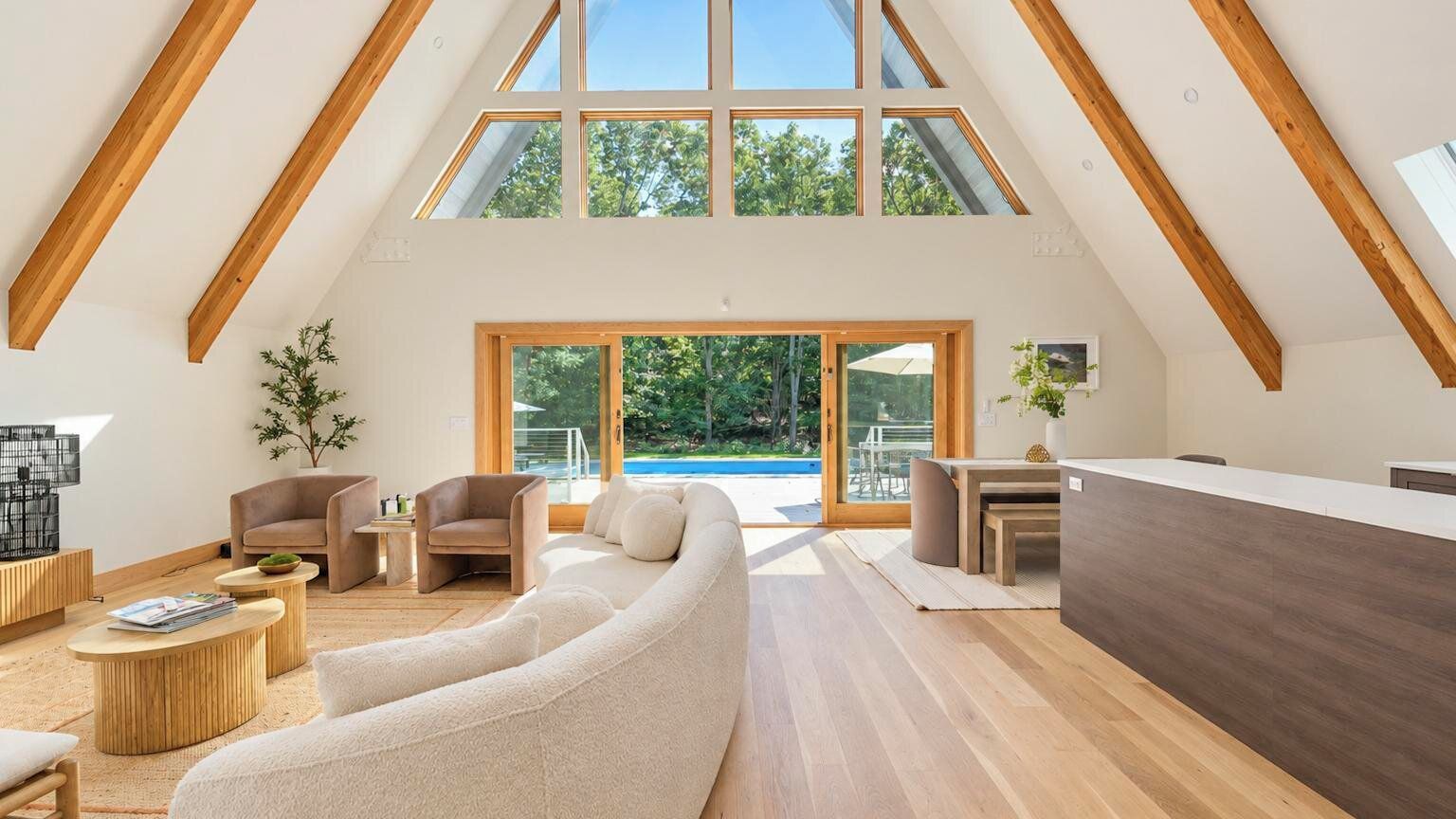 A spacious loft with a high ceiling, wooden beams, a large window, and a view of the outdoors.