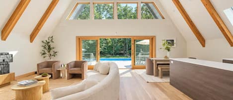 A spacious loft with a high ceiling, wooden beams, a large window, and a view of the outdoors.