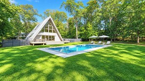 A modern house with a triangular roof, a swimming pool, and a deck with lounge chairs.