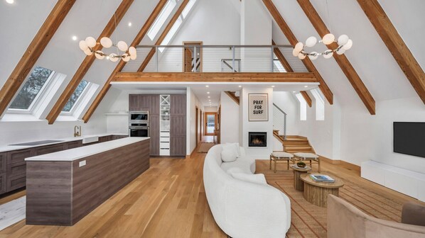 A spacious loft with a high ceiling, wooden beams, a kitchen with modern appliances, a cozy seating area, and a fireplace.