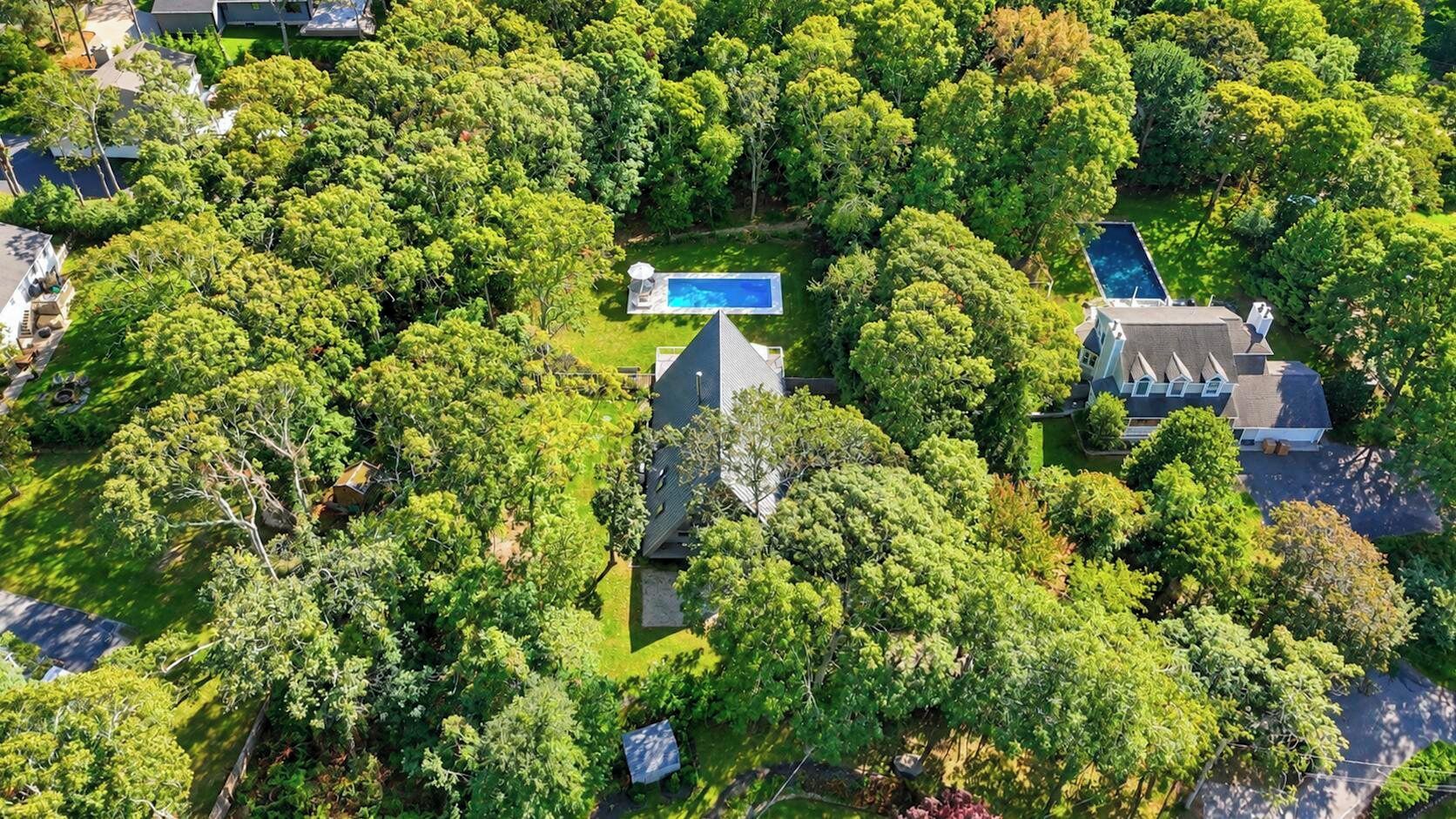 An aerial view of a residential area with multiple houses, a swimming pool, and lush greenery.