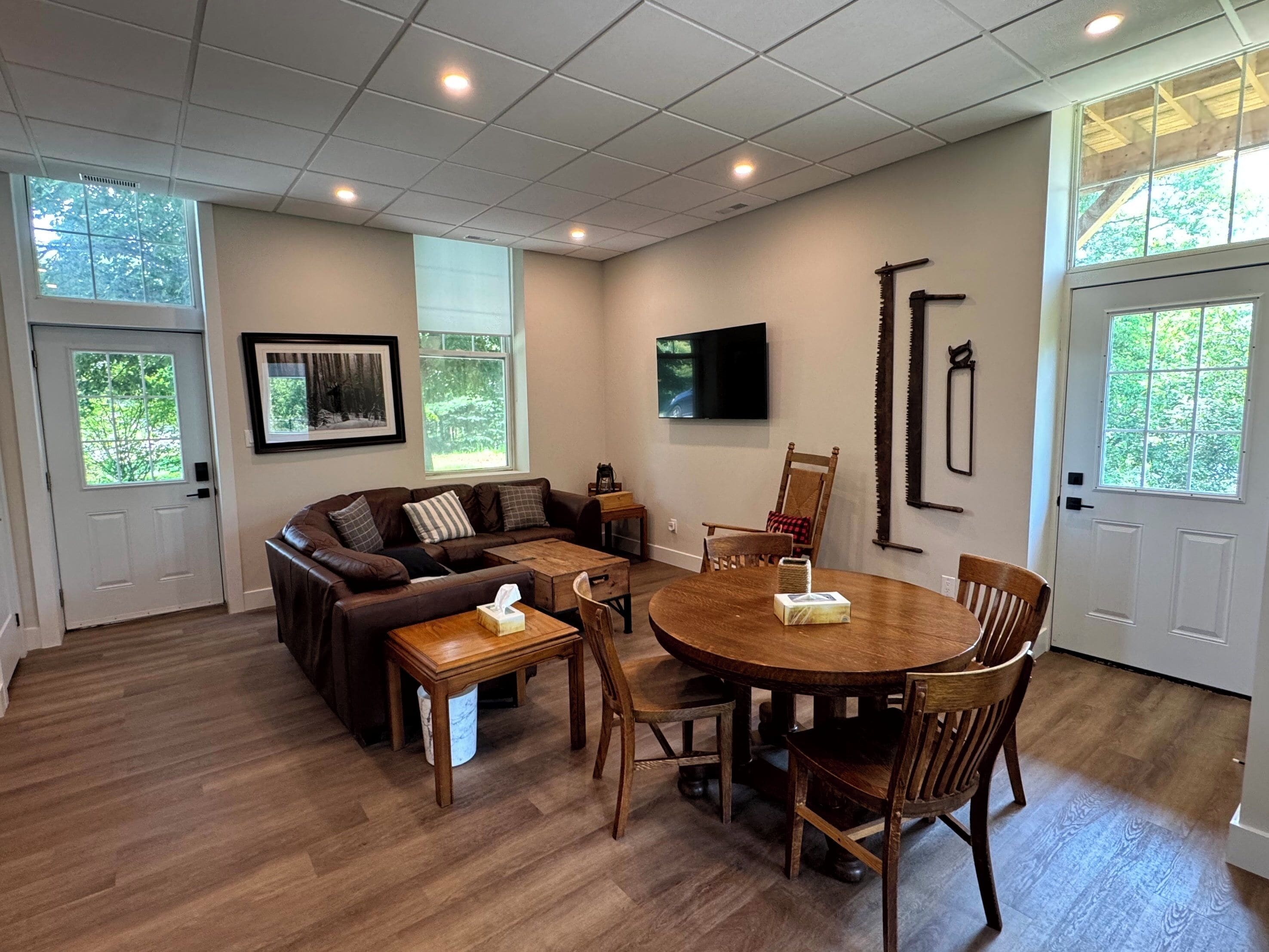 A living room with a sectional sofa, a round dining table, and a TV mounted on the wall.