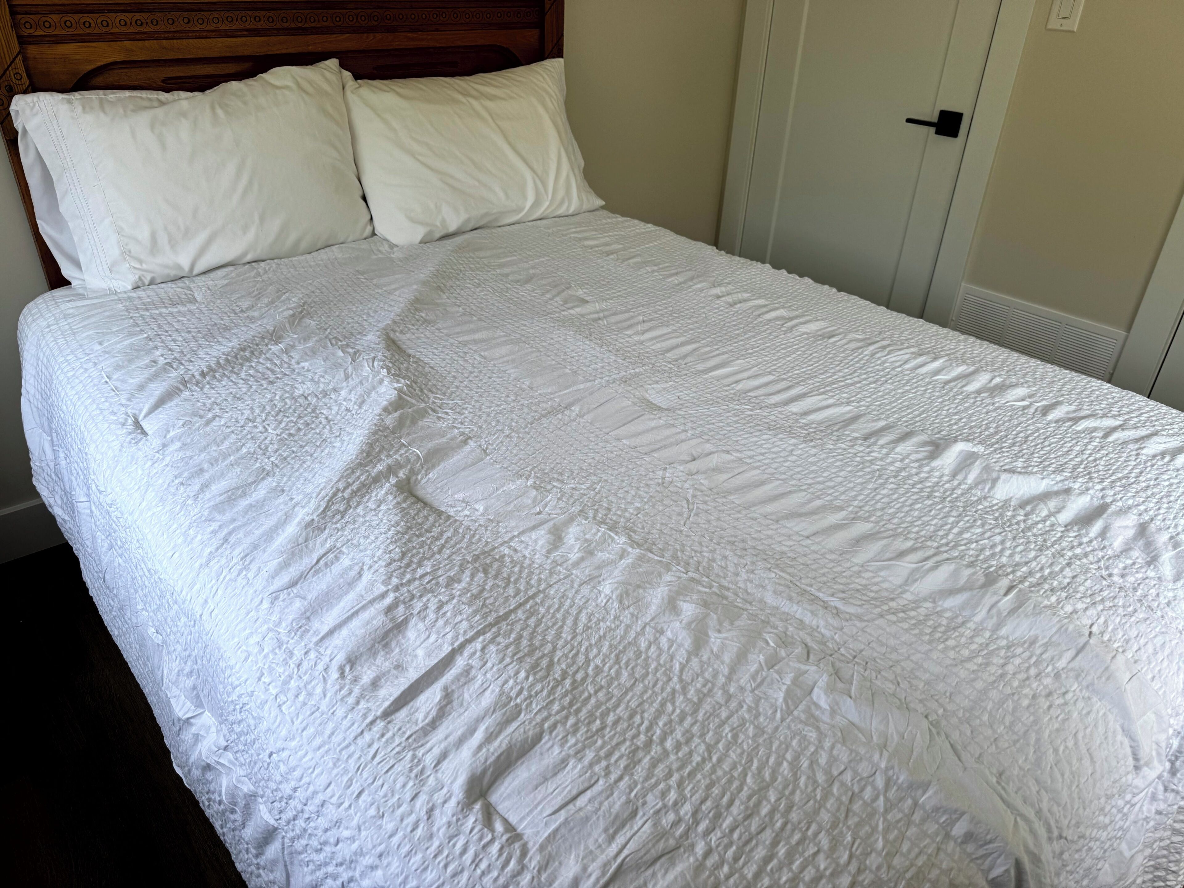 A neatly made bed with a white quilted bedspread and two pillows.
