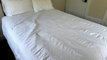 A neatly made bed with a white quilted bedspread and two pillows.