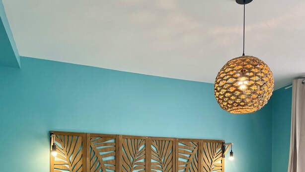 A room with two beds, a wooden headboard with leaf patterns, a hanging light fixture, and a small wooden table.