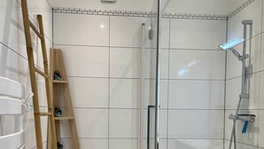 A modern bathroom with a glass-enclosed shower, a wooden ladder, and a tiled floor.