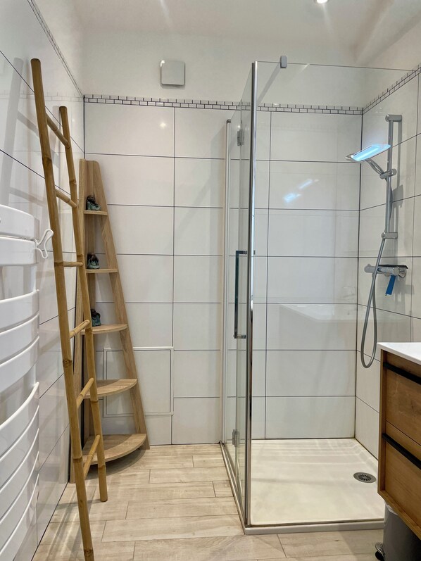 A modern bathroom with a glass-enclosed shower, a wooden ladder, and a tiled floor.