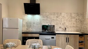 A modern kitchen with a dining area. It includes a refrigerator, stove, microwave, and sink. There are wicker chairs and a table set for dining.