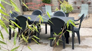 An outdoor patio with a table and chairs, surrounded by greenery and a stone wall.