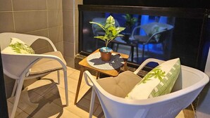 Una habitación pequeña y moderna con dos sillas blancas, una mesita con una planta en maceta y un televisor sobre un mueble.