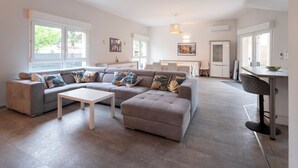 Ein modernes Wohnzimmer mit einem grauen Ecksofa, einem weißen Couchtisch und einem Essbereich mit weißem Tisch und Stühlen.