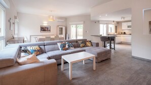 Ein modernes Wohnzimmer mit einem Ecksofa, einem weißen Couchtisch und einem Essbereich mit Tisch und Stühlen.
