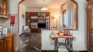 Una cocina con piso de mármol, armarios de madera, un televisor y un comedor con una mesa preparada para dos.