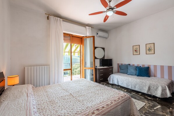 Un dormitorio con dos camas, un ventilador de techo, un televisor y una ventana con cortinas.