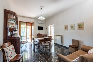 Un coin repas avec une table et des chaises en bois, un téléviseur fixé au mur et une fenêtre avec des rideaux.