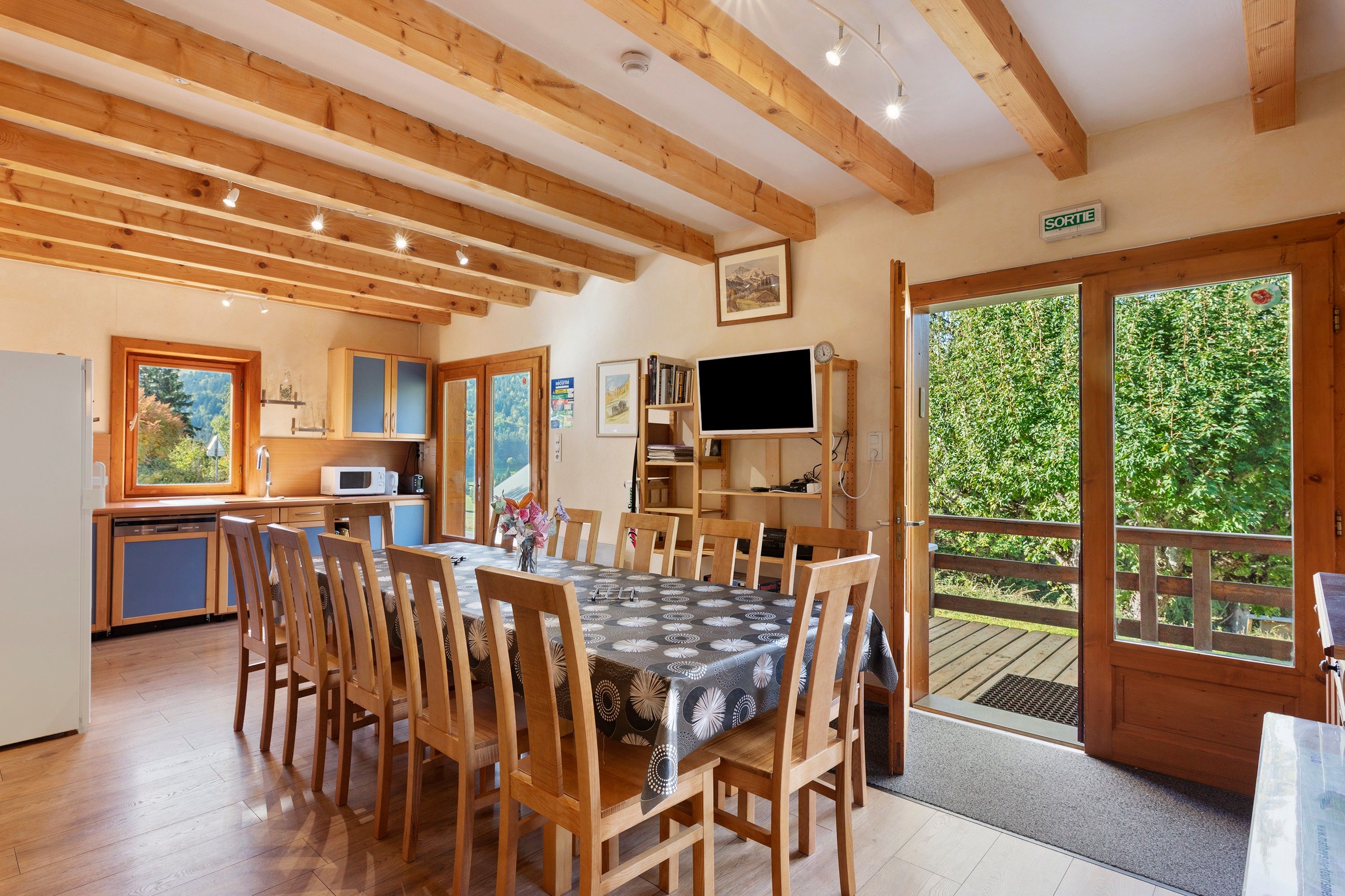 A cozy wooden interior with a dining area, kitchen, and a large window offering a view of greenery.