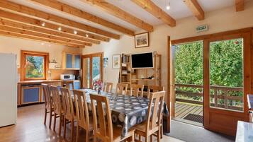 A cozy wooden interior with a dining area, kitchen, and a large window offering a view of greenery.