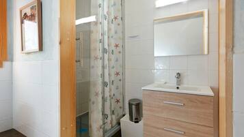 Une salle de bain équipée d’une douche, d’un lavabo, d’un miroir et d’une poubelle.