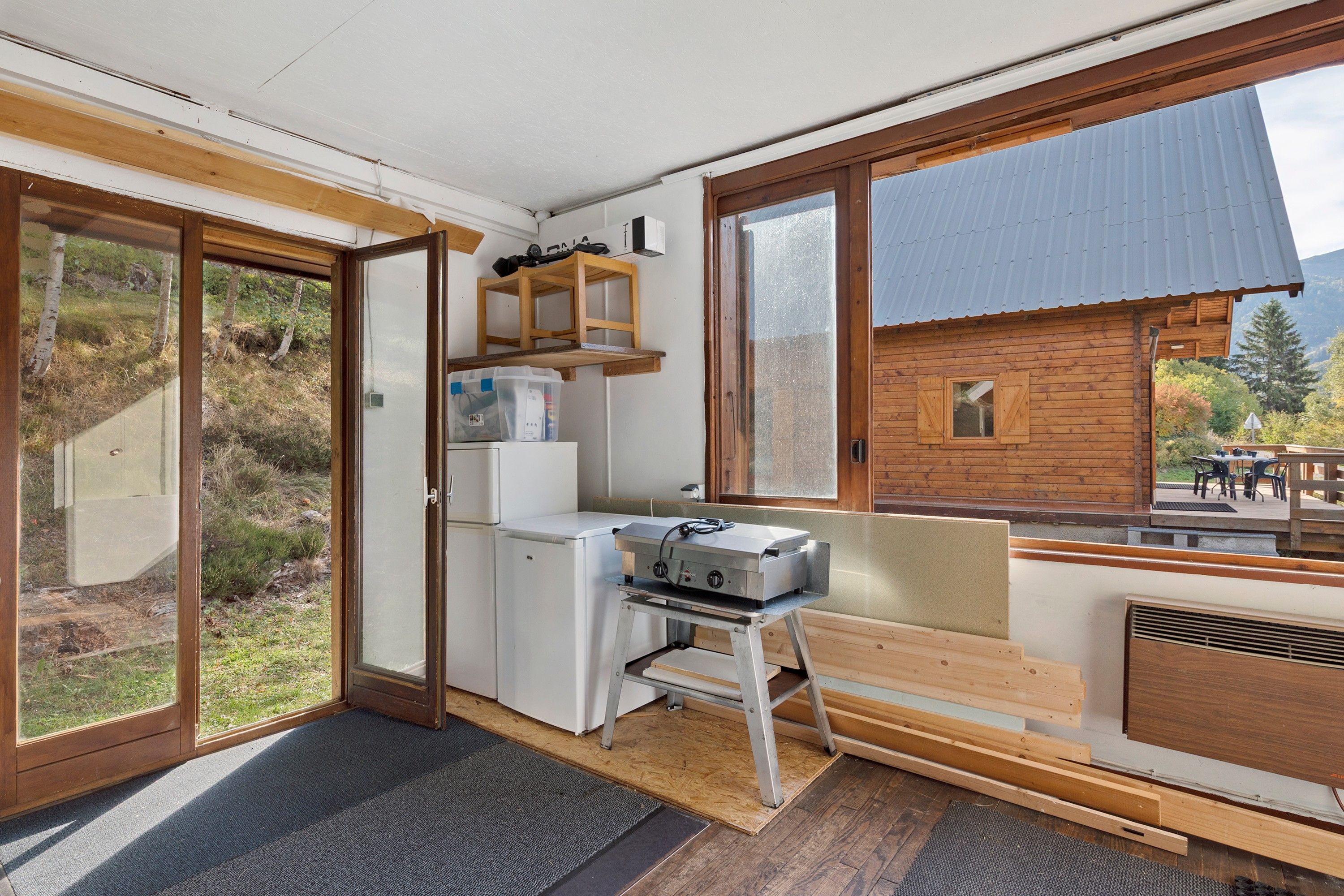 A compact kitchen with a built-in refrigerator, a portable stove, and a wooden bench.