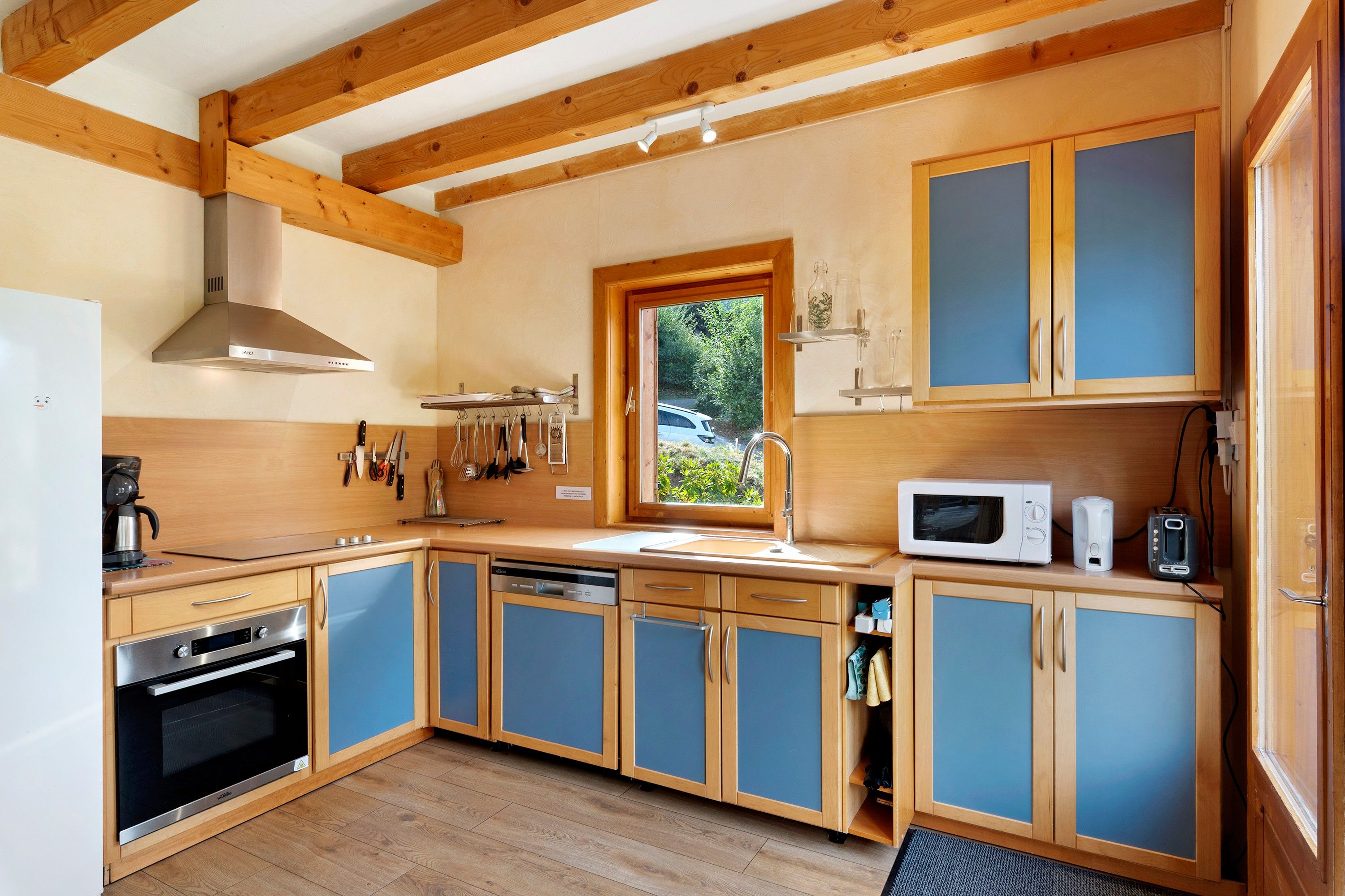 Une cuisine compacte avec des meubles en bois, un four encastré, un four à micro-ondes et une fenêtre donnant sur un espace verdoyant.