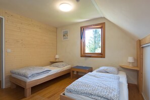 A room with two wooden beds, a small table, a window, and a wall-mounted picture. - Mountain Chalet for 13 Guests (La Morte)