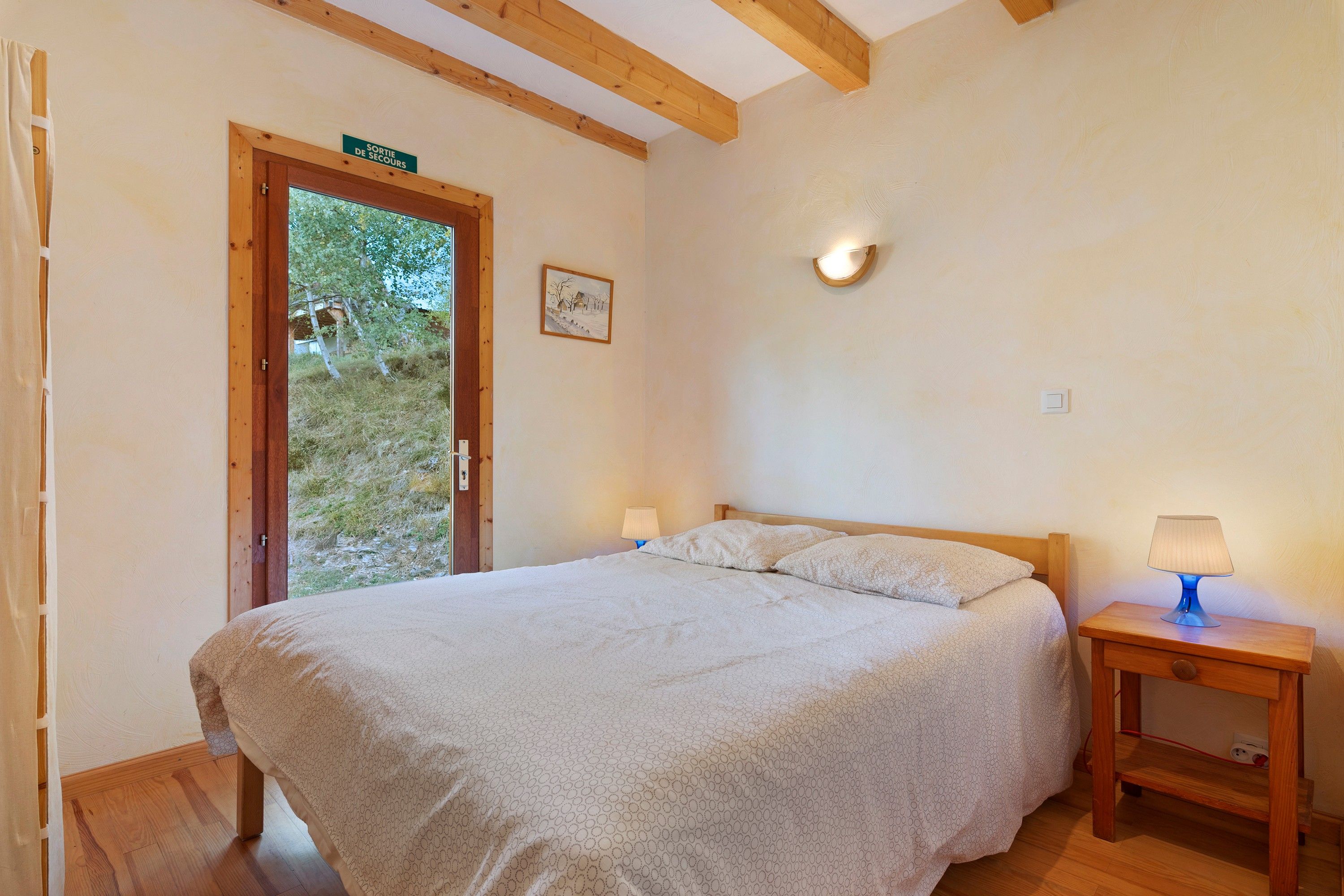 Ein Schlafzimmer mit einem Bett, Nachttischlampen, einem Holznachttisch, einer Tür mit einem Schild und einer an der Wand befestigten Leuchte.