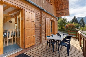 A wooden cabin with a deck, a table with chairs, and a door leading to an interior room.
