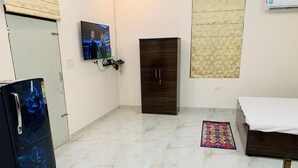 Ein Zimmer mit Marmorboden, einem dunklen Holzschrank, einem an der Wand befestigten Fernseher und einem Kühlschrank mit floralem Dekor.