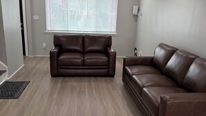 A modern living room with a brown leather sofa, a window with blinds, and a ceiling-mounted air conditioner. - Peaceful cozy 3-bedroom house with AC in Queens. (Queens)