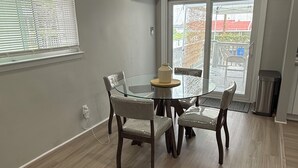 A dining area with a round glass table and four chairs, a vase on the table, and a sliding glass door leading outside. - Peaceful cozy 3-bedroom house with AC in Queens. (Queens)