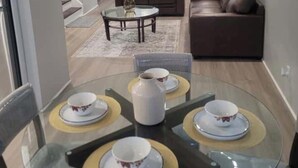 A modern living room with a glass dining table set for four, a brown leather sofa, and a coffee table. - Peaceful cozy 3-bedroom house with AC in Queens. (Queens)