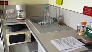 Una kitchenette compacta con cafetera, una botella y un papel sobre la encimera.