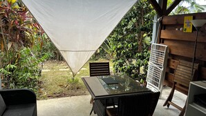A covered outdoor seating area with a table and chairs, surrounded by lush greenery and a wooden fence. - KAYLI DOUDOU LECARBET PEACEFUL VACATIONS IN A QUIET ENVIRONMENT (LE CARBET)