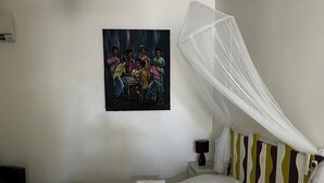 Una cama bien hecha con ropa blanca y un plaid verde, un dosel blanco y un cuadro de personas en la pared.