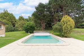 Ein rechteckiger Swimmingpool mit integriertem Rutsche, umgeben von einer gepflasterten Liegefläche.