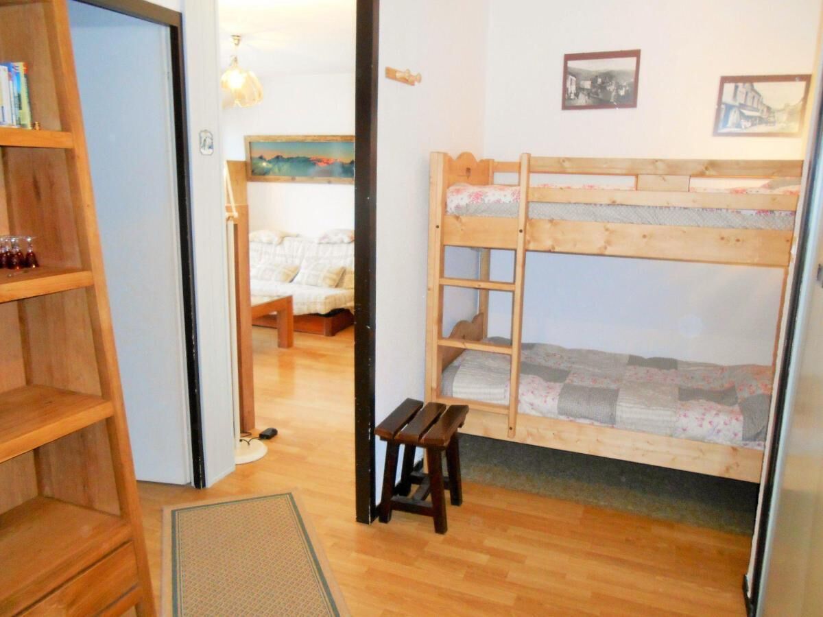 Ein Zimmer mit einem Etagenbett, einem Holzregal und einem kleinen Hocker.
