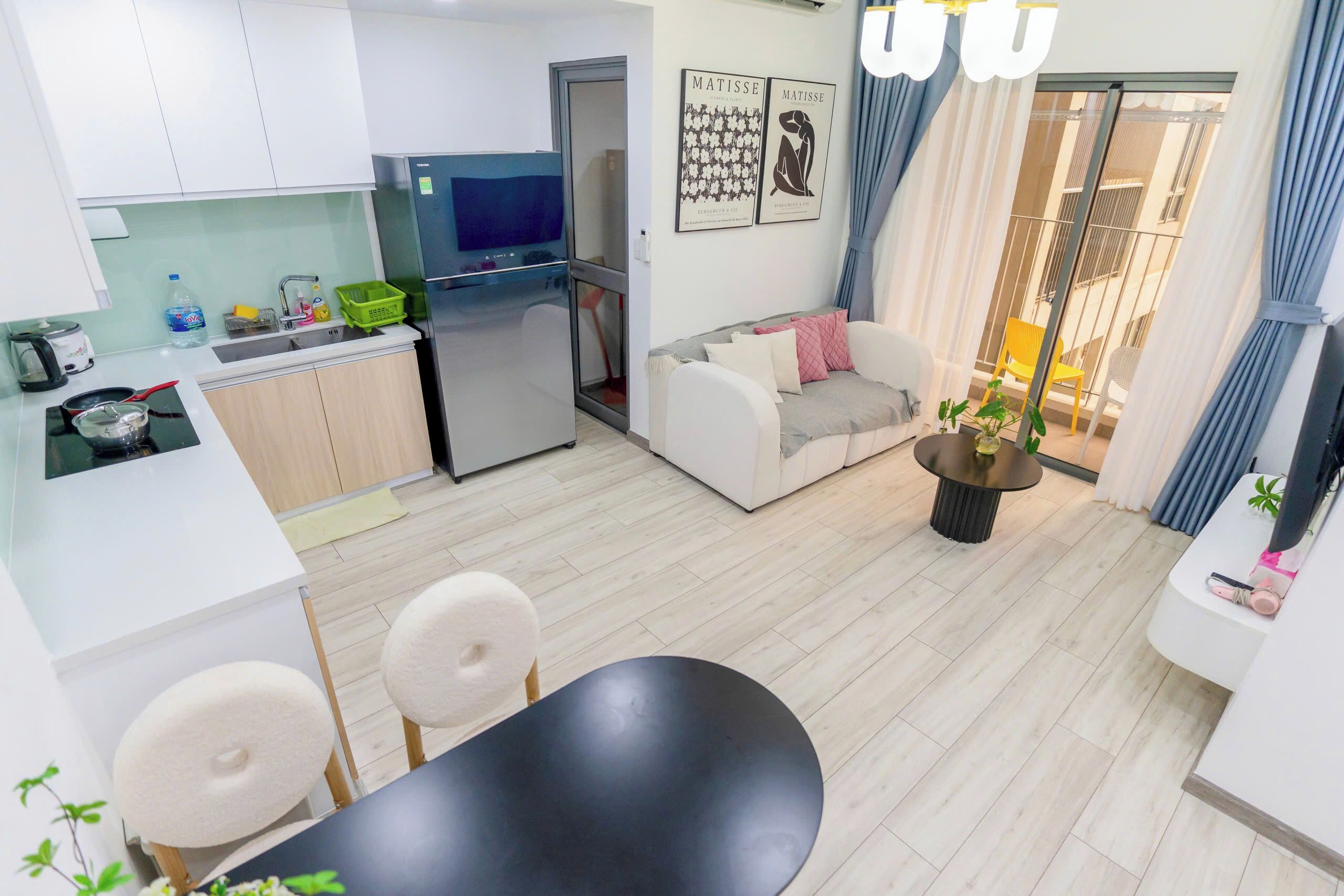 A compact living space with a kitchenette, a dining area, a sofa, and a balcony with curtains.