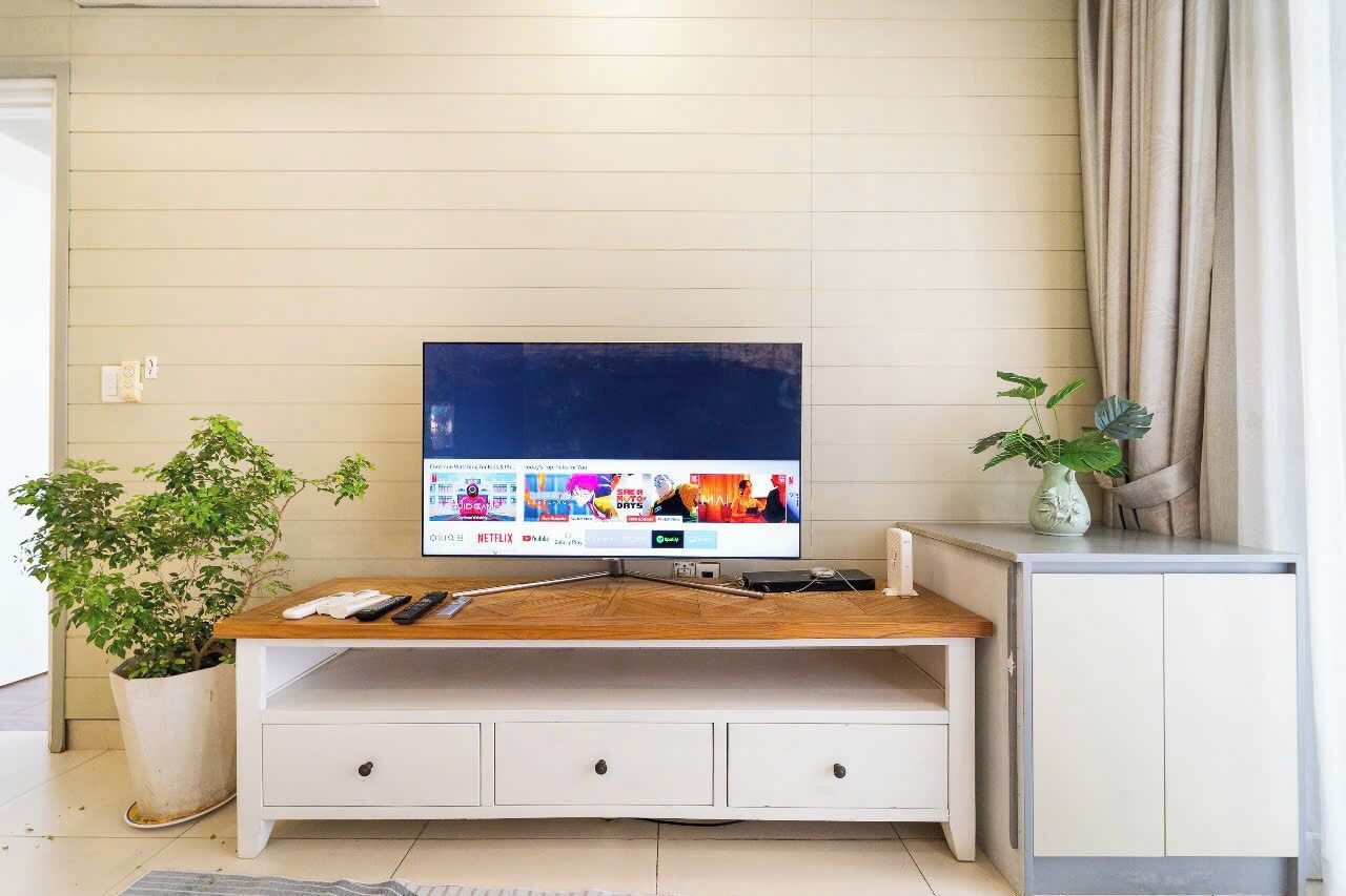 A living room with a TV on a wooden stand, a white cabinet, and a potted plant.