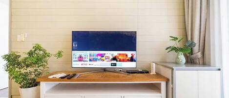 A living room with a TV on a wooden stand, a white cabinet, and a potted plant.