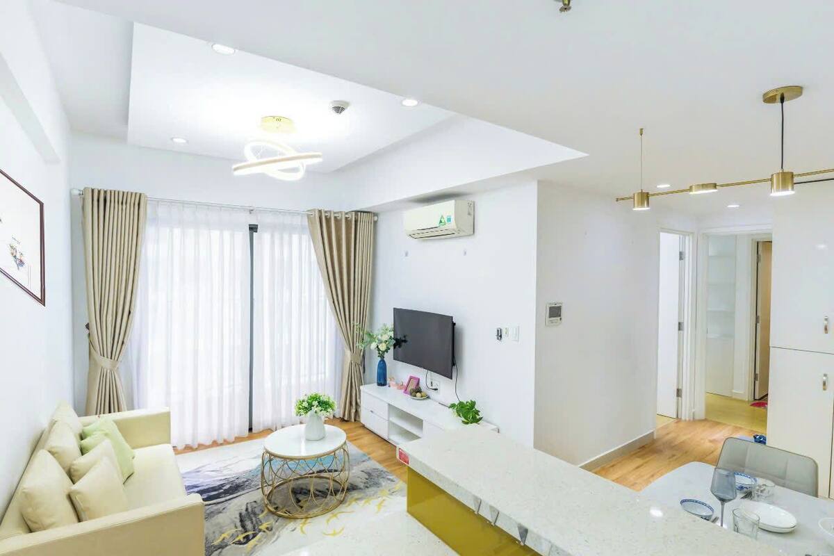 A modern living room with a sofa, a coffee table, a flat-screen TV, and a dining area with a table and chairs.