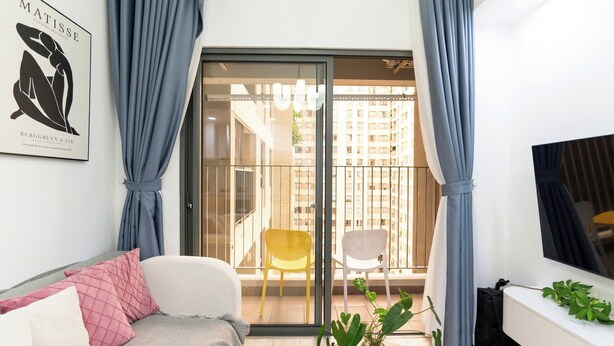 A modern living room with a sofa, a coffee table, a TV, and a balcony with a view of buildings. - Cherry Houses - Masteri Thao Dien (Ho Chi Minh City)