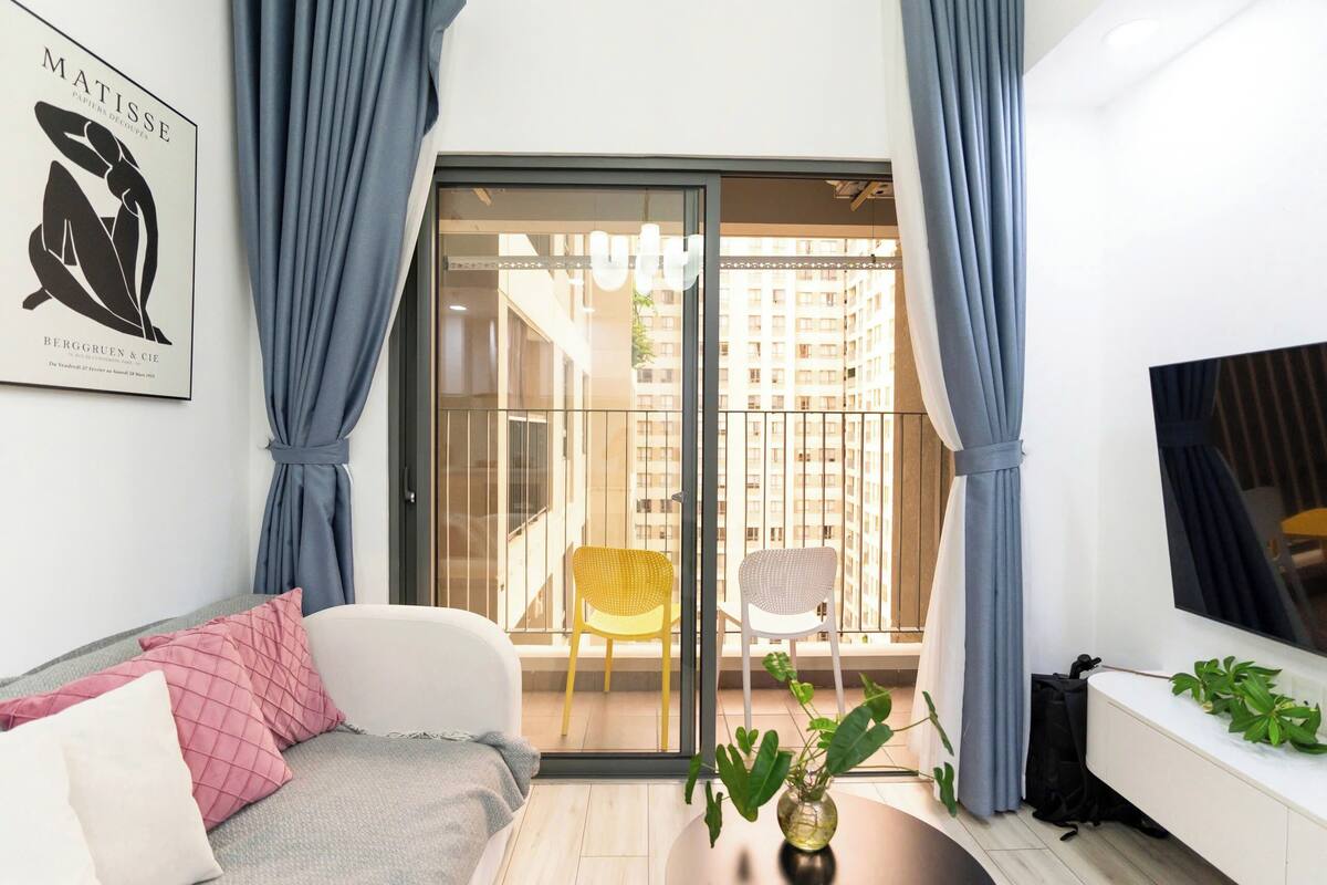 A modern living room with a sofa, a coffee table, a TV, and a balcony with a view of buildings.