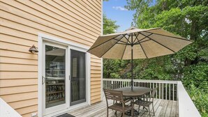 A wooden deck with a table and chairs, an umbrella, and a sliding glass door.