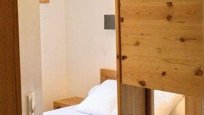 Un lit superposé en bois avec un matelas et des oreillers blancs, un luminaire suspendu et un cadre de porte en bois.