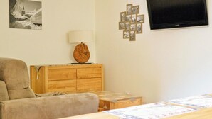 Une pièce comprenant un canapé, un meuble en bois avec une lampe, un téléviseur fixé au mur et un ensemble de photos encadrées.
