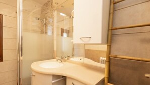 Un baño con cabina de ducha de vidrio, lavamanos curvo y espejo sobre él.