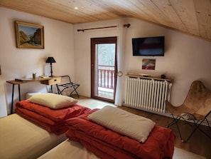 A bedroom with two beds, a desk, a chair, a radiator, and a TV.