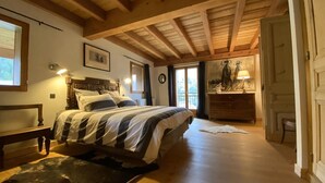 A bedroom with a wooden ceiling, a bed with striped bedding, a dresser, and a lamp.