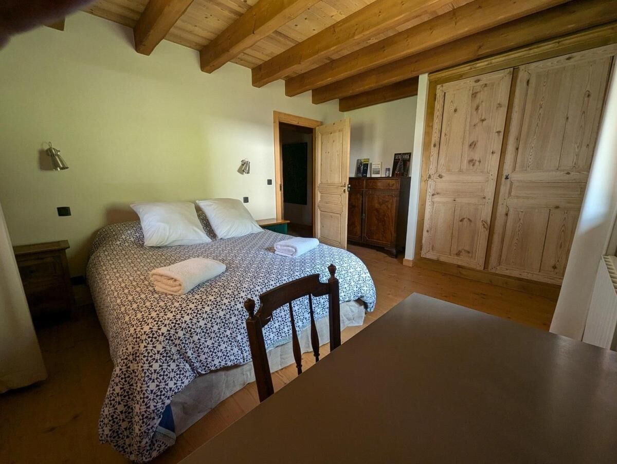 A bedroom with a bed, wooden headboard, a wooden table, and a wardrobe.